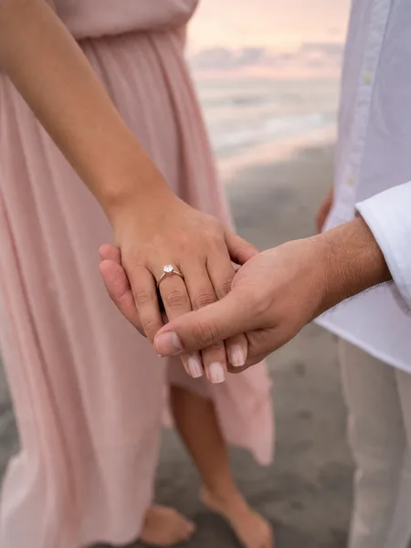 Close-up of hands showing off engagement ring on a quiet morning beach, romantic engagement photos.