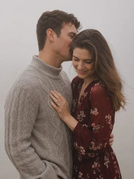 Intimate whisper in ear on a foggy sea cliff, couple in floral dress and sweater, engagement photos