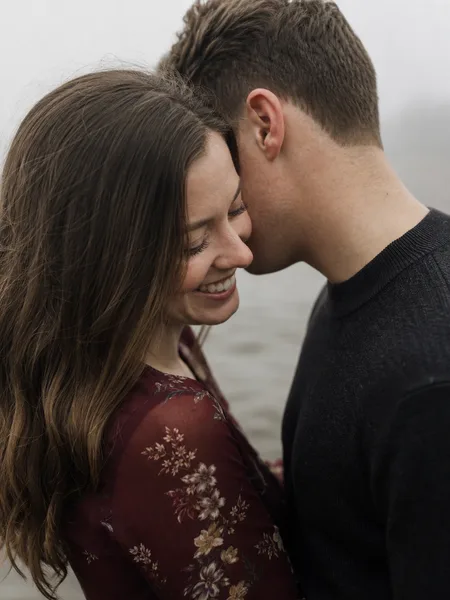 Extreme close-up of a couple, he whispers in her ear, standing in foggy beach water, floral midi dress, engagement photos