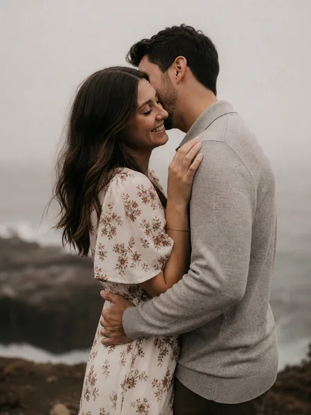 Close-up of couple whispering on foggy sea cliff, floral dress, intimate moment, engagement photos.