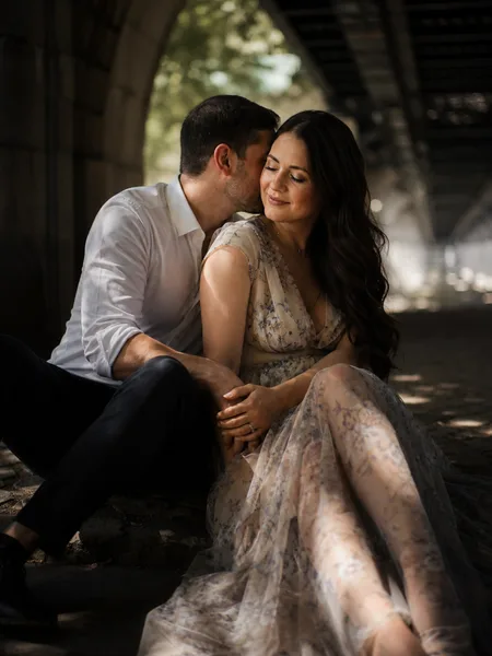 Close-up of a couple whispering on a bridge, dappled sunlight on floral dress, engagement photos