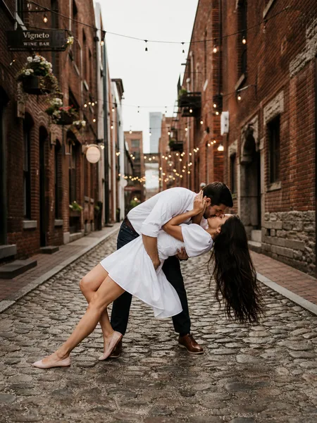 Groom dipping bride for a kiss in a brick alley, playful engagement photos.