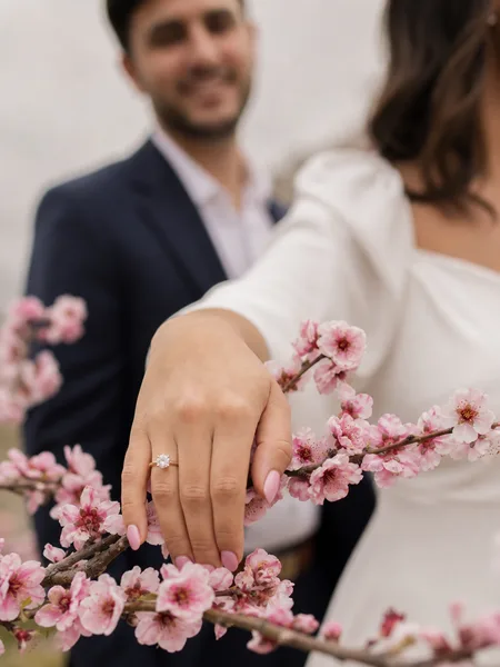 Close-up of an engagement ring on a cherry blossom branch, white dress sleeve, engagement photos