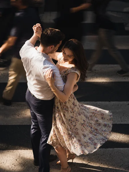 Engagement photos: Couple slow-dancing on a crosswalk in dramatic midday shade, floral dress twirling, dappled sunlight.