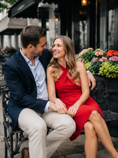 Couple sitting close on bench by cafe, bright dress, overcast light, engagement photos