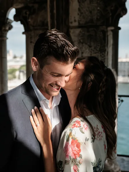 Close-up profile of couple as she whispers in his ear on historic bridge with dramatic shadows, engagement photos.