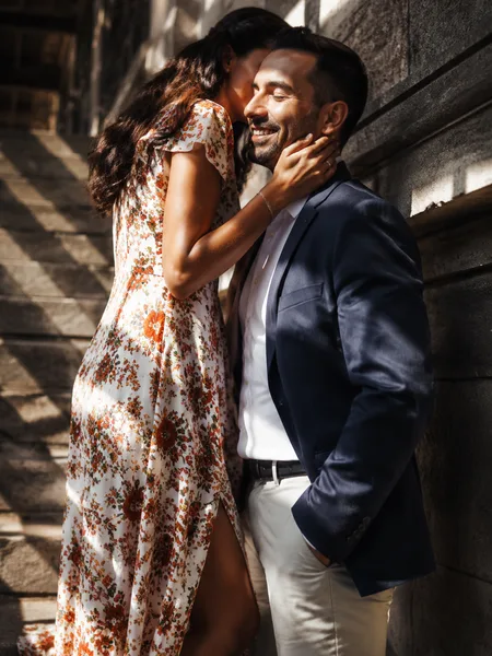 Woman in floral dress whispering to partner on shadowy city staircase, engagement photos