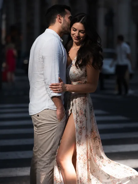 Engagement photos: Intimate whisper in ear on a crosswalk, floral dress, harsh midday shadow creating contrast.