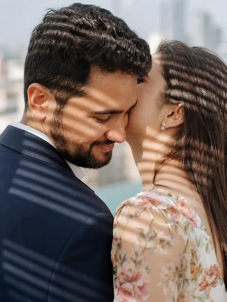 Close-up of woman whispering in man's ear on a rooftop, floral dress, engagement photos