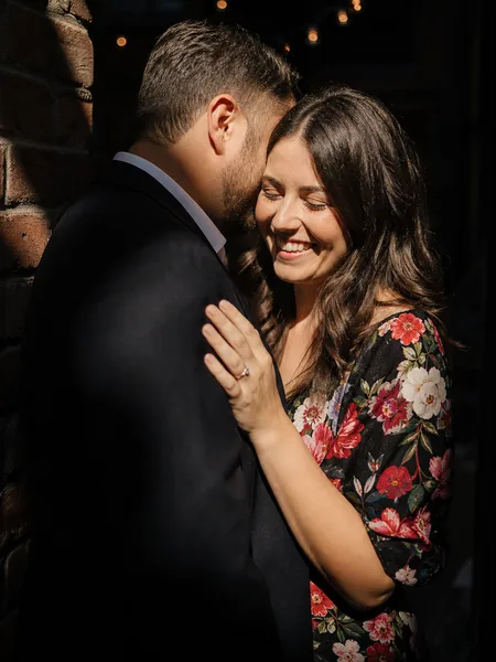 Groom whispering to bride in a sunlit patch of a brick alley, engagement photos.