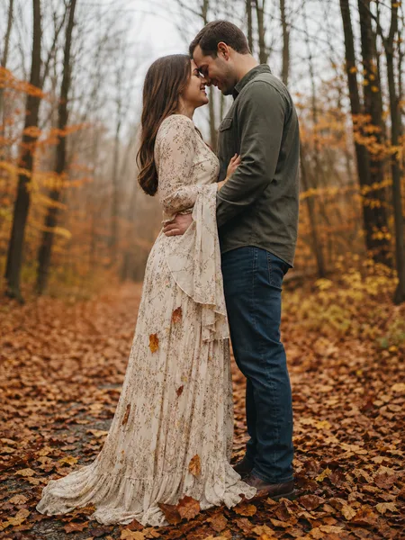 Close-up of a couple with foreheads touching, standing on a path covered in red and orange autumn leaves, engagement photos.