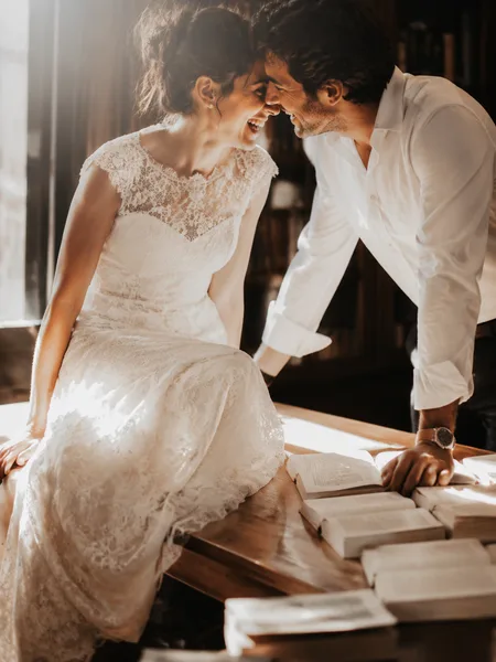 Couple candidly laughing in grand library, white elegant attire, dramatic side light, romantic engagement photos.