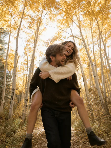 Piggyback ride in aspen grove, woman in cream knit dress, soft afternoon light, engagement photos