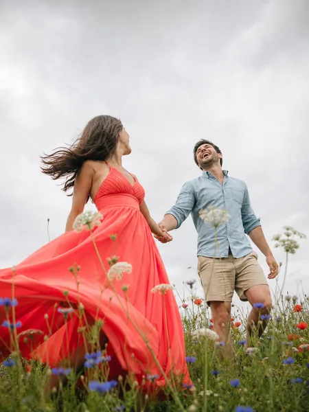 Candid laughing couple twirling in a bright dress in a wildflower meadow for engagement photos.