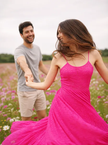 Woman spinning in bright dress in wildflower meadow overcast day, man laughing in engagement photos