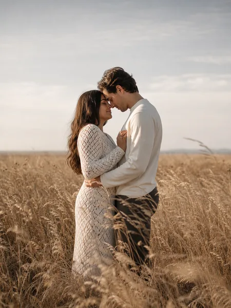 Couple with foreheads touching, eyes closed, in a field of dried tall grass under soft afternoon light, engagement photos.