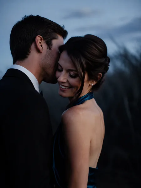 Close-up of a groom whispering to his bride in a dark prairie at blue hour, engagement photos.
