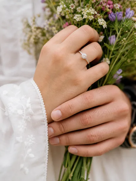 Close up of engagement ring on hand with wildflower stems, white embroidered dress cuff, engagement photos