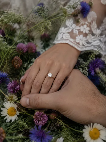 Top-down view of hands with ring amid wildflowers, white dress, editorial style, engagement photos.