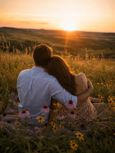 Couple sitting close in a flowering prairie at sunset, engagement photos.