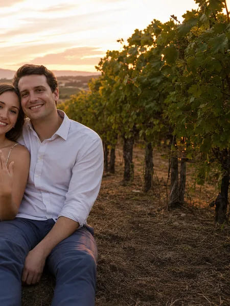 Couple sitting on the ground in a vineyard at sunset, floral dress, warm light, engagement photos