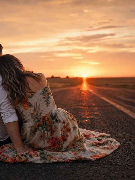 Couple sitting on road at sunset, floral dress, warm light, country horizon, engagement photos.