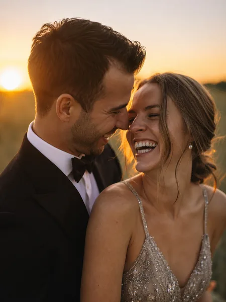 Couple laughing in formal wear at sunset on grassy lawn, golden light, engagement photos.