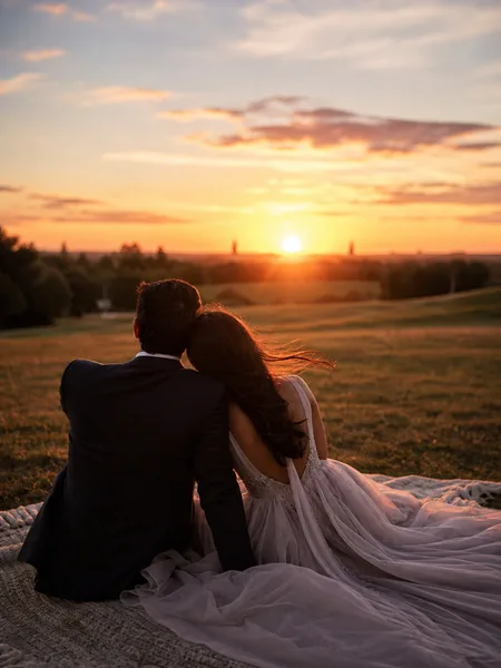 Couple sitting close on a blanket at sunset in a grassy park, engagement photos
