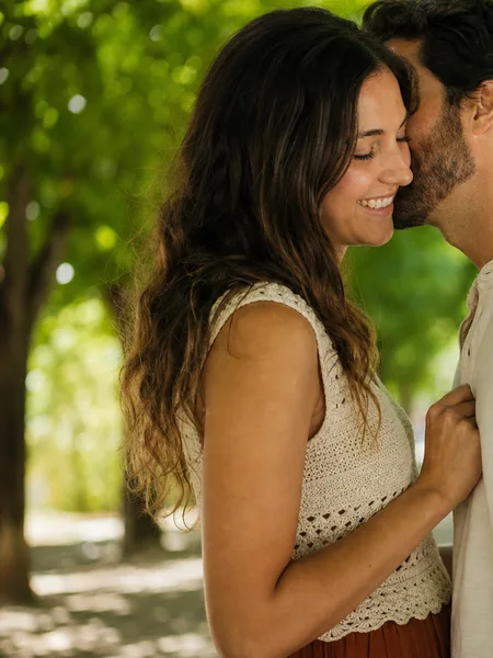 Close-up of a couple whispering together under a bright spring tree canopy, engagement photos.